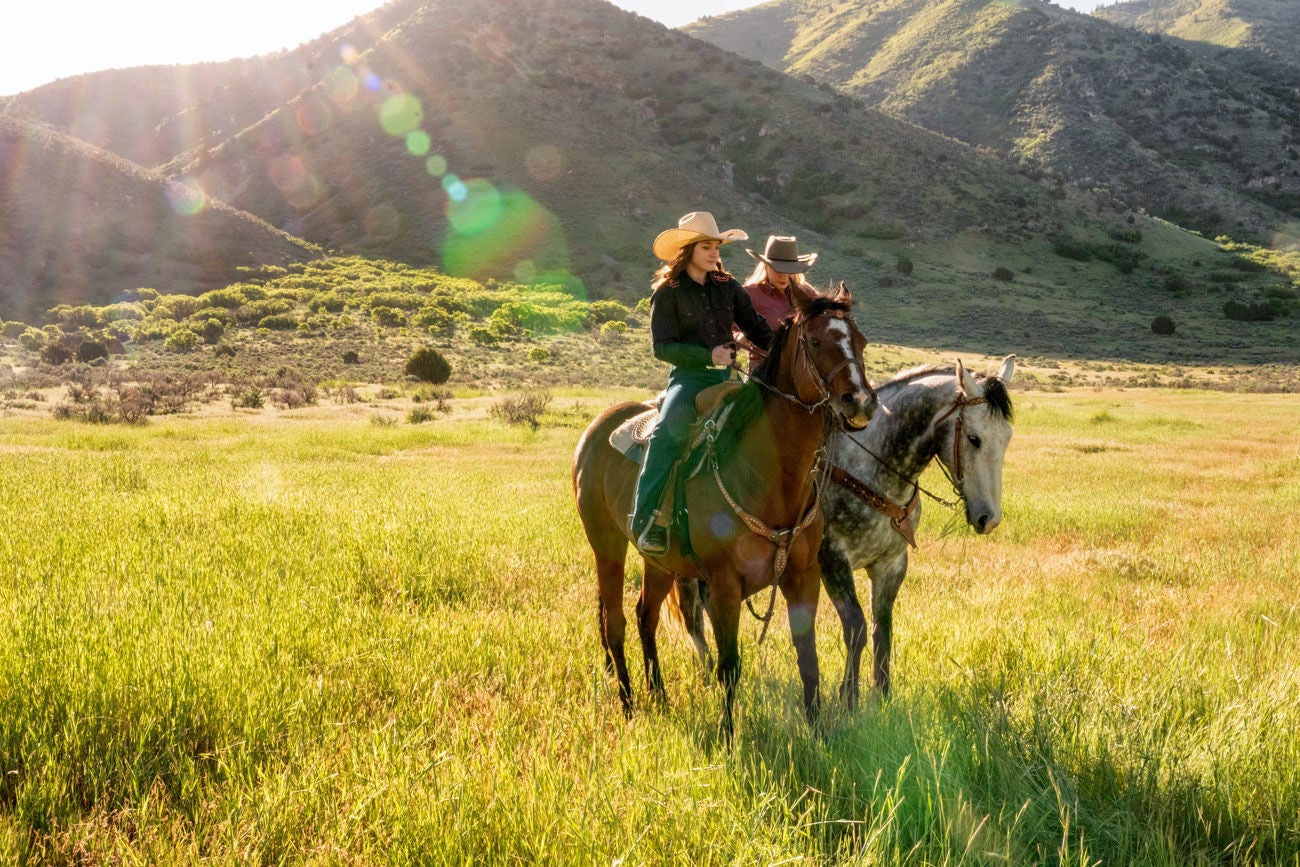 Two young adult women on horseback, riding through a meadow on a cattle ranch in rural Utah
